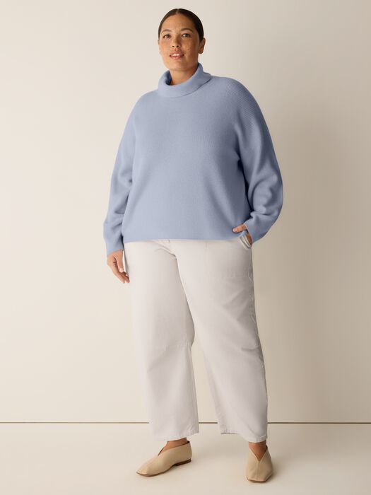 Light blue turtleneck ribbed knit sweater with relaxed fit, worn with white wide-leg pants, front view