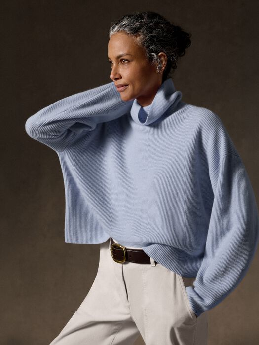 Oversized ribbed turtleneck sweater in light blue, worn with white trousers and brown belt