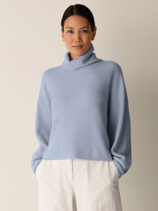 Oversized ribbed turtleneck sweater in light blue, front view on model with white trousers