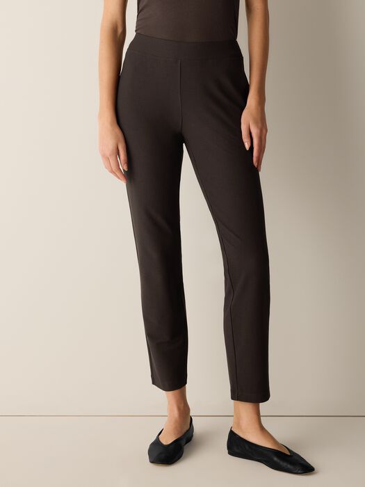 Slim-fit dark brown ankle-length trousers with elastic waistband, worn with black ballet flats