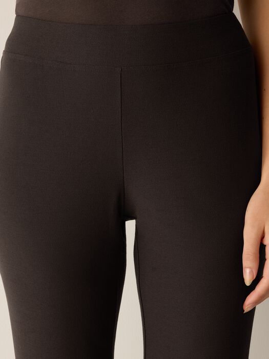 Close-up of dark brown slim pants with wide elastic waistband, worn on model, front view