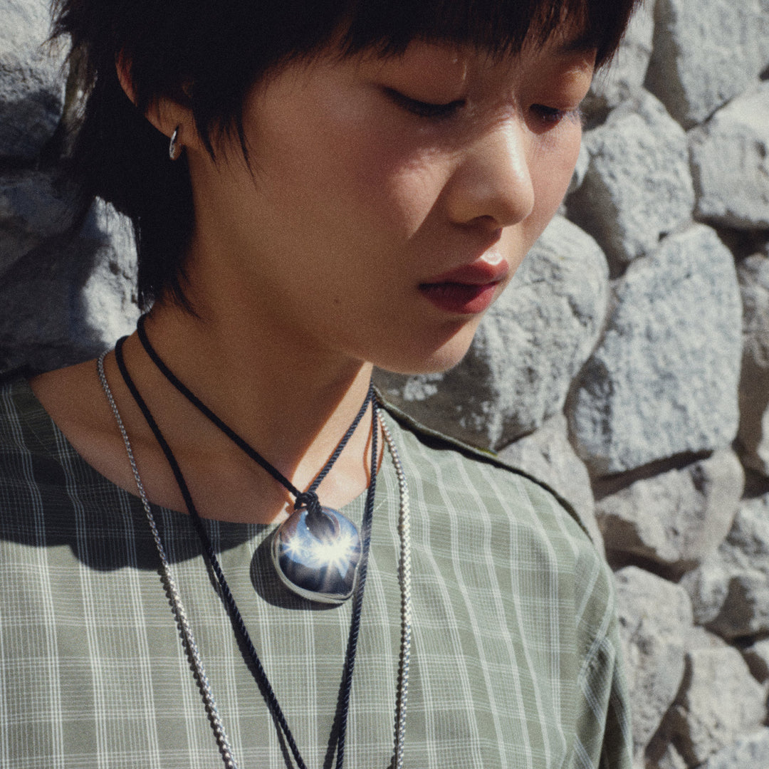 Layered pendant necklaces with dark circular charm worn over striped shirt