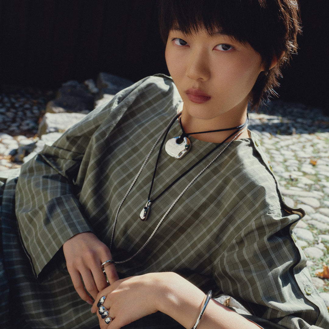 Layered pendant necklaces with silver chains and black cord ties worn by model