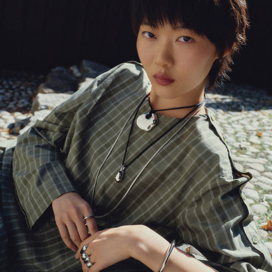 Layered pendant necklaces with silver chains and black cord ties worn by model