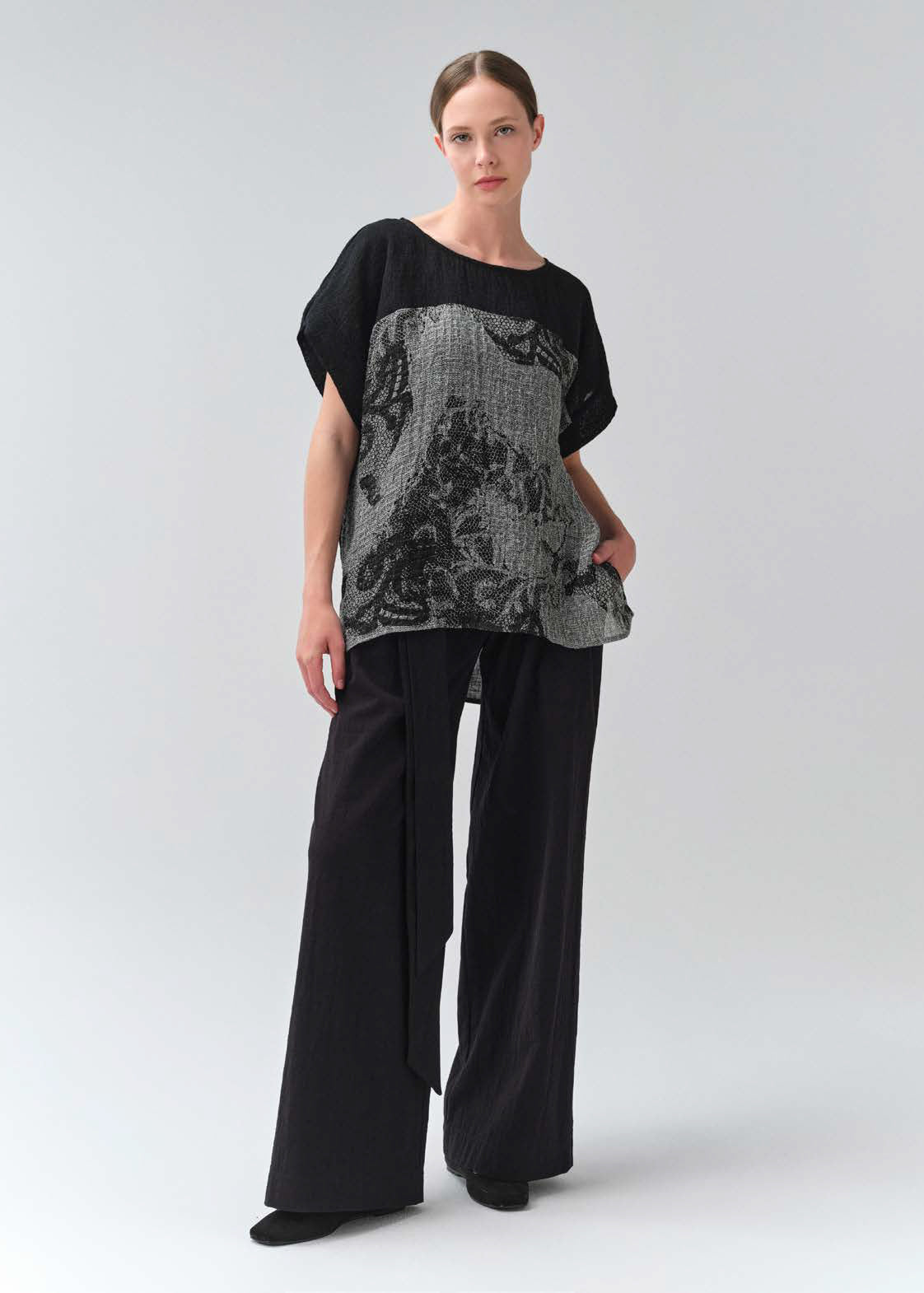 Woman wearing a black and gray patterned top with wide-leg pants on a white background