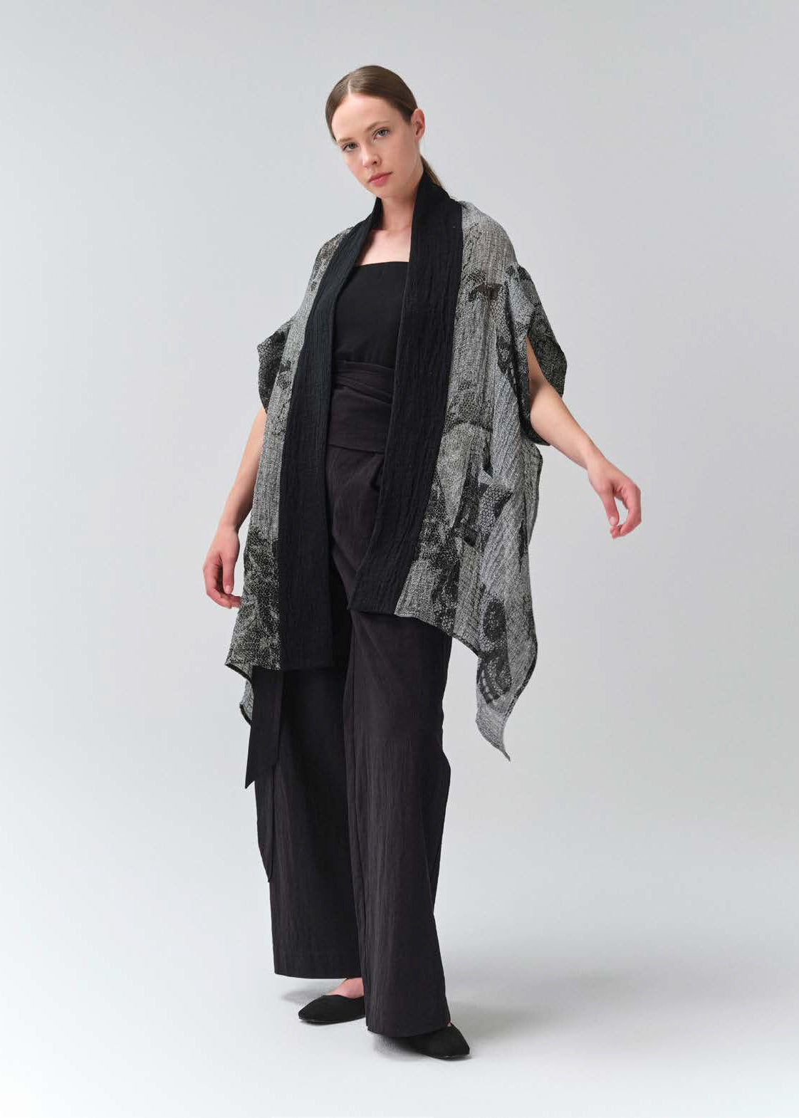 Woman wearing a black outfit with a patterned gray shawl on a white background
