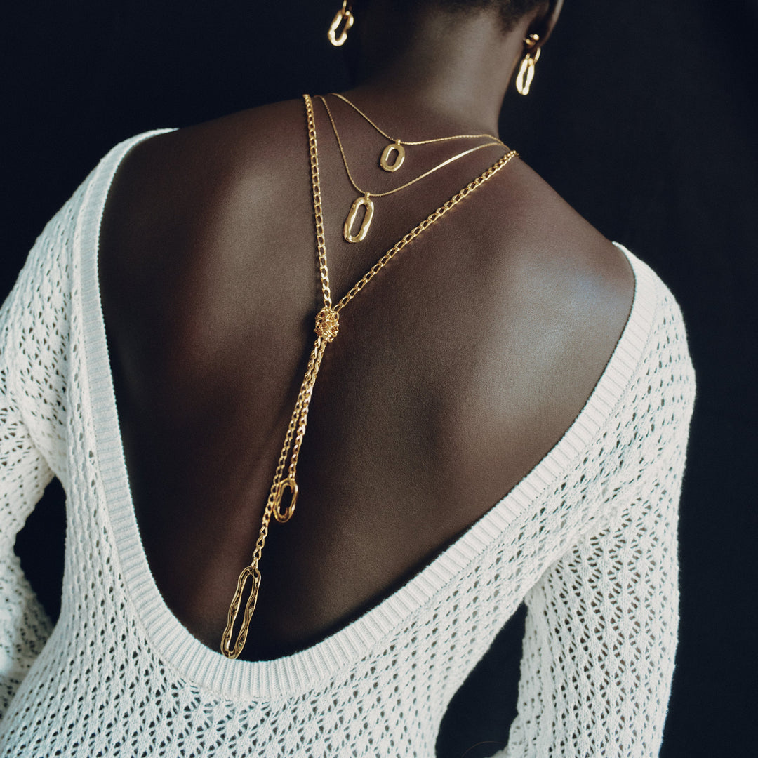 Layered gold chain necklaces on model wearing white open-back sweater