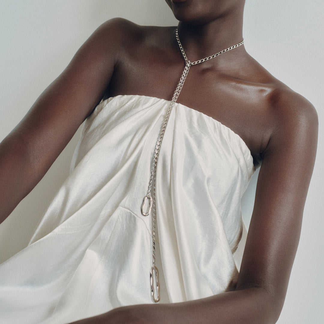 Long chain lariat necklace with oval pendant worn by model in white draped top