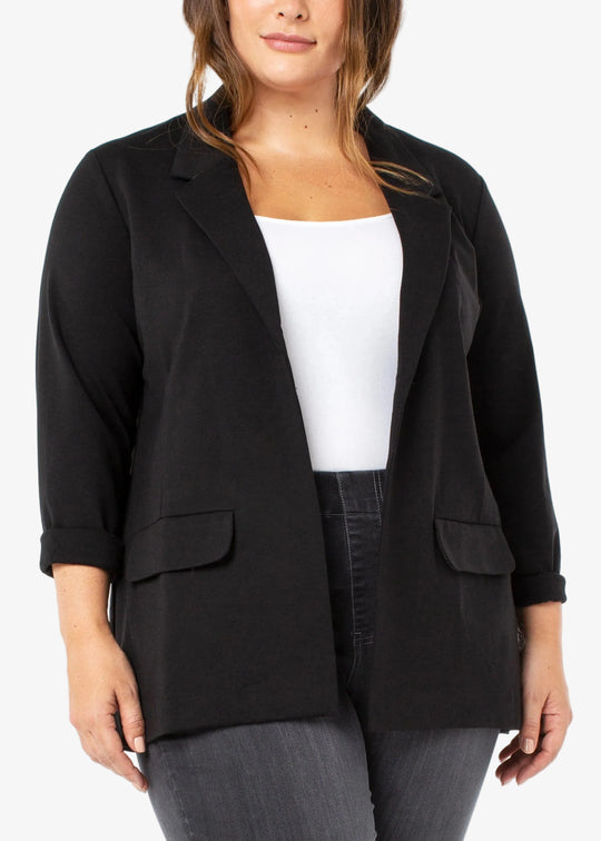 Woman wearing a black blazer over a white top and gray pants on a white background