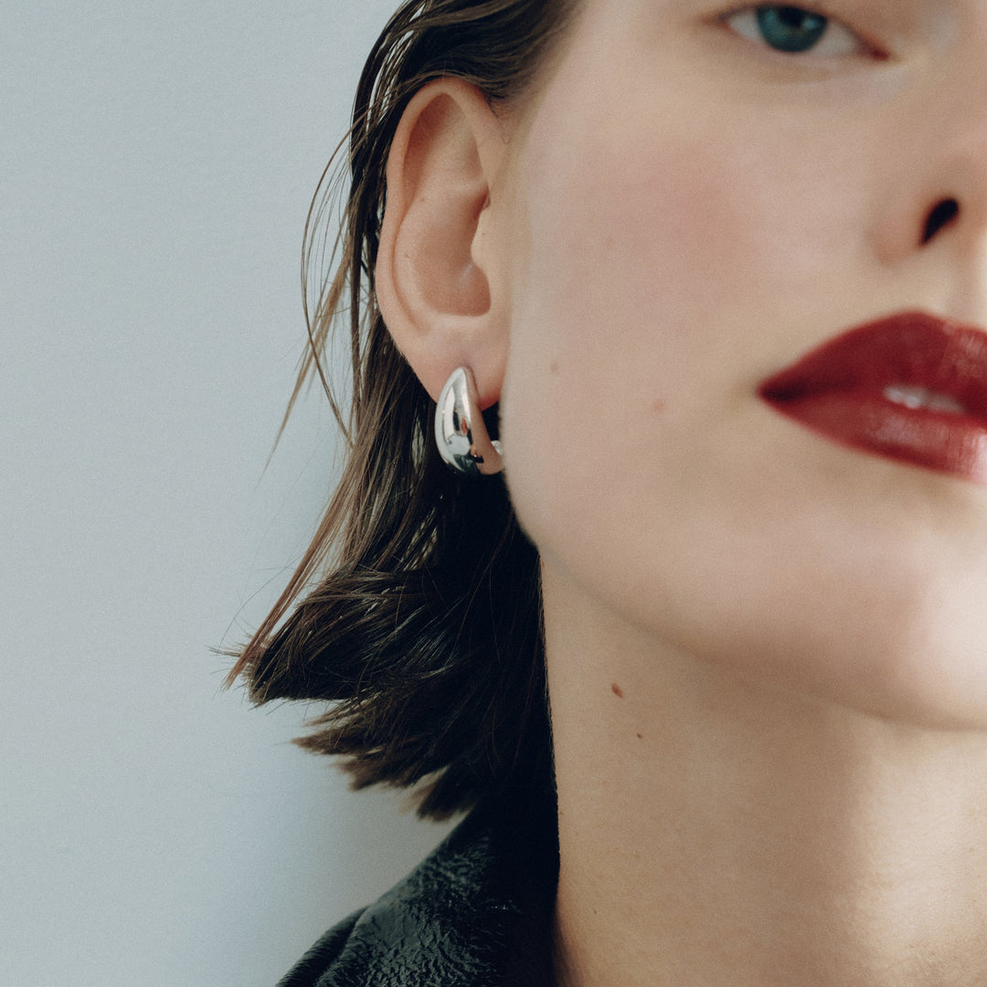 Small silver hoop earring worn on model's ear, chunky rounded design