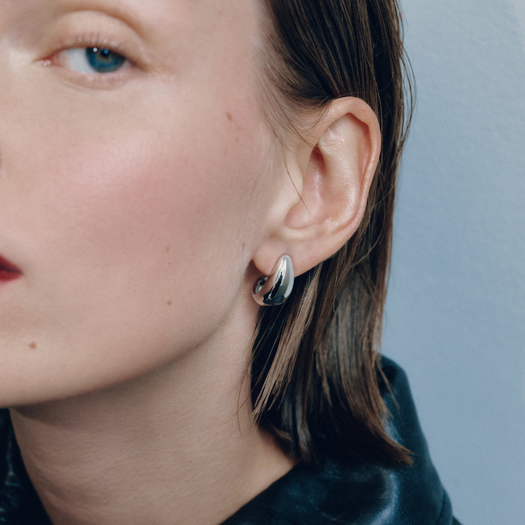 Small chunky silver hoop earrings worn on model, showing thick rounded design