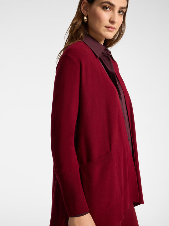 Red draped cardigan with open front, long sleeves, and side pocket detail