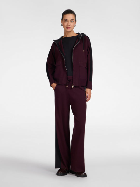 Dark maroon hooded zip cardigan with drawstring hood and zip front, worn with trousers