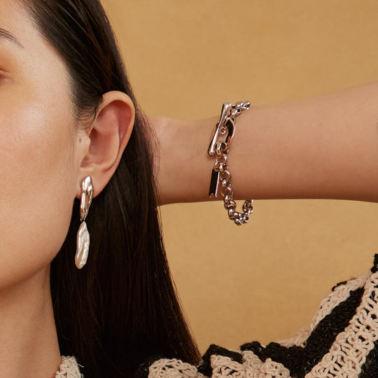 Silver chain bracelet with toggle clasp worn on wrist, styled with matching drop earrings
