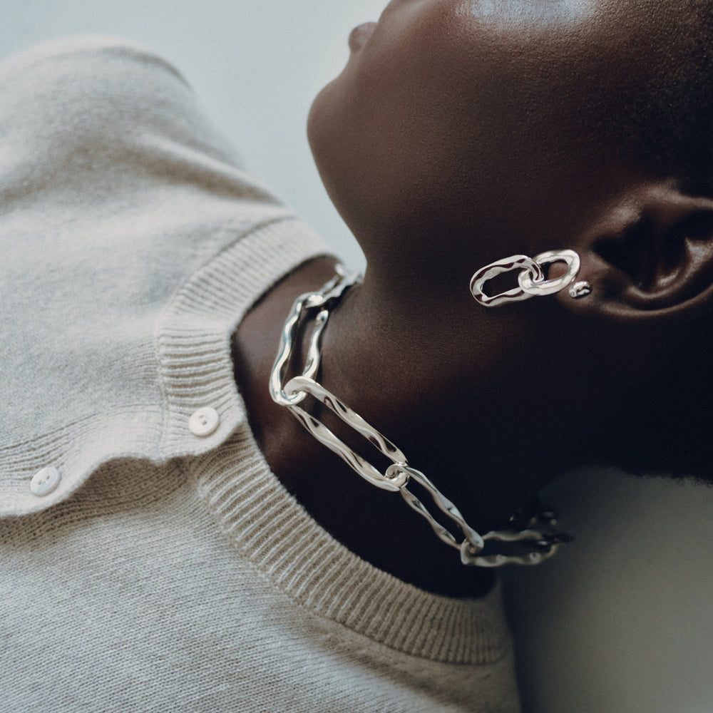Silver chainlink collar necklace worn by model in cream cardigan, profile view