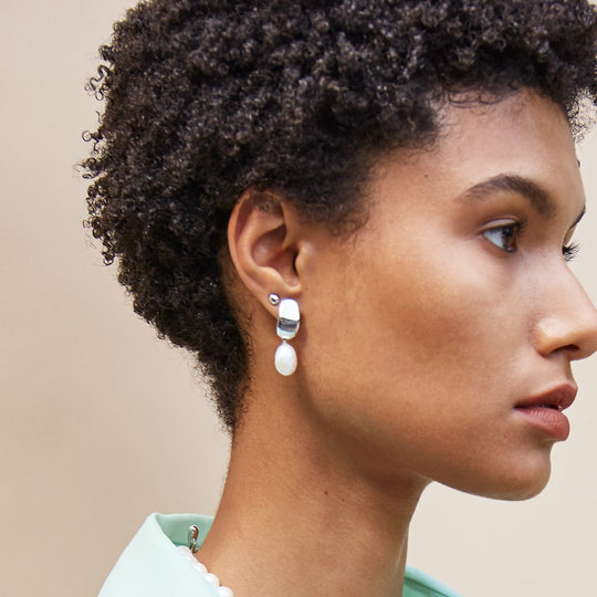 Drop earrings with silver geometric tops and white pearl dangles worn by model