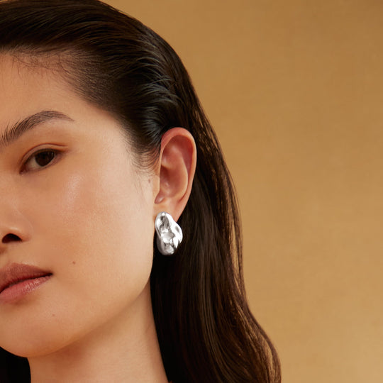 Silver molten-style stud earring worn on model's ear, irregular organic shape