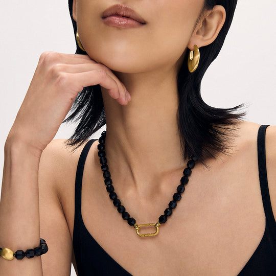 Black faceted beaded necklace with gold oval carabiner clasp pendant, worn on model