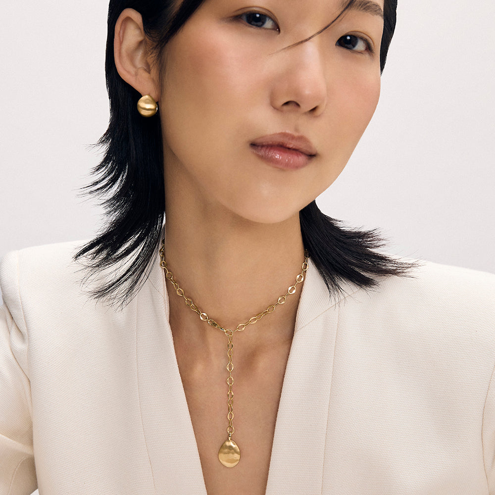Gold lariat necklace with oval chain links and disc pendant, worn with matching gold dome earrings