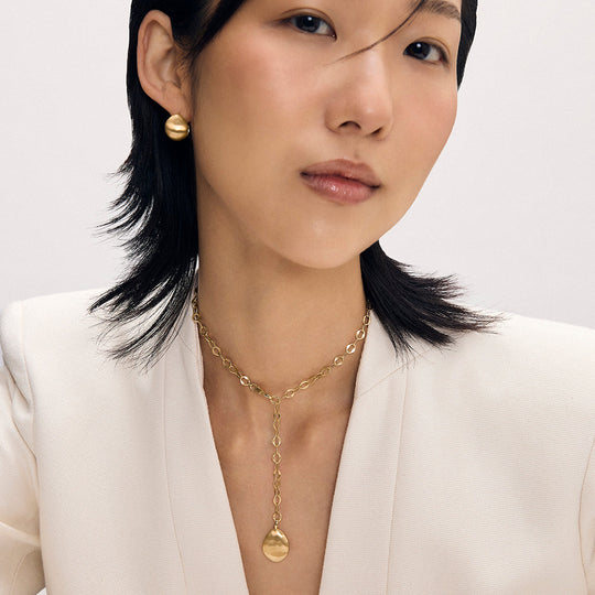 Gold lariat necklace with oval chain links and disc pendant, worn with matching gold dome earrings
