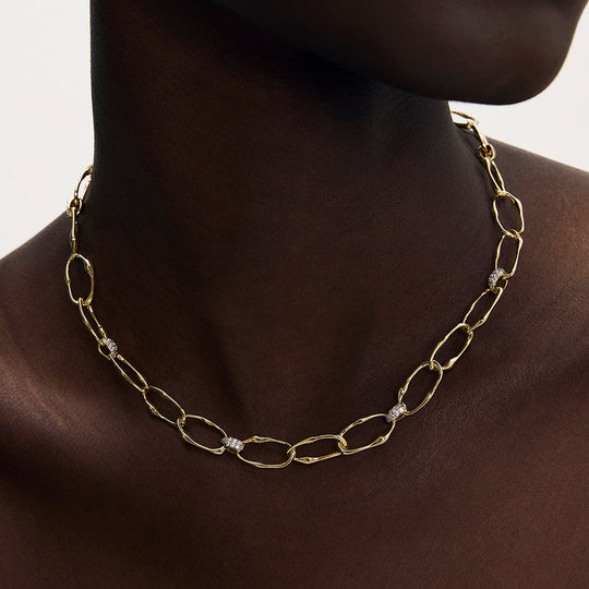 Gold oval link chain necklace with diamond pavé connectors worn on a model's neck