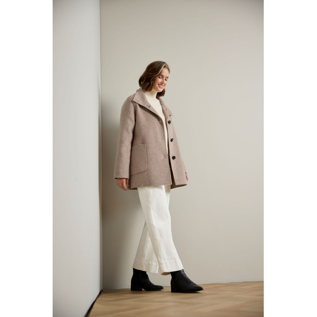 Oversized taupe wool coat with patch pocket and dark buttons, worn over white trousers and black boots