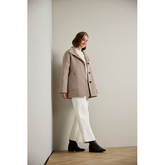 Oversized taupe wool coat with patch pocket and dark buttons, worn over white trousers and black boots