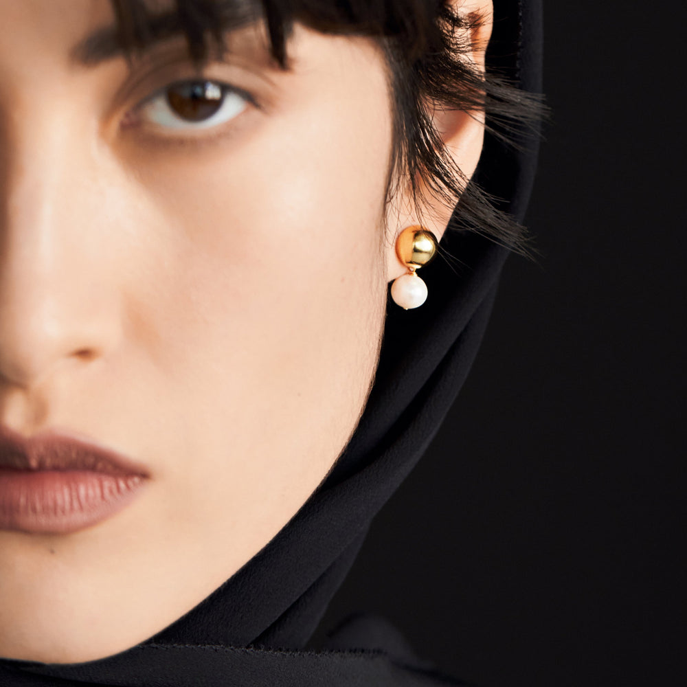 Gold stud earrings with white pearl drops worn by model with dark hair