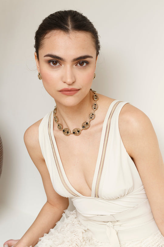 Gold filigree medallion necklace with black stones worn by model in white dress