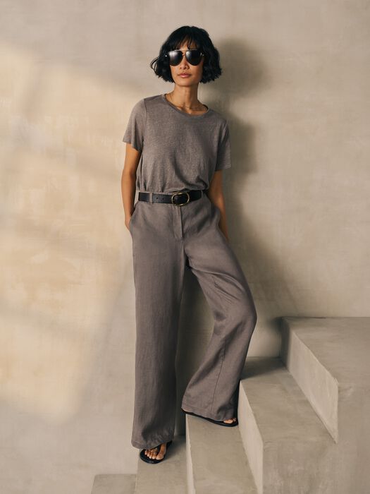 Woman wearing wide-leg high-waisted linen trousers with belt in gray-brown tone