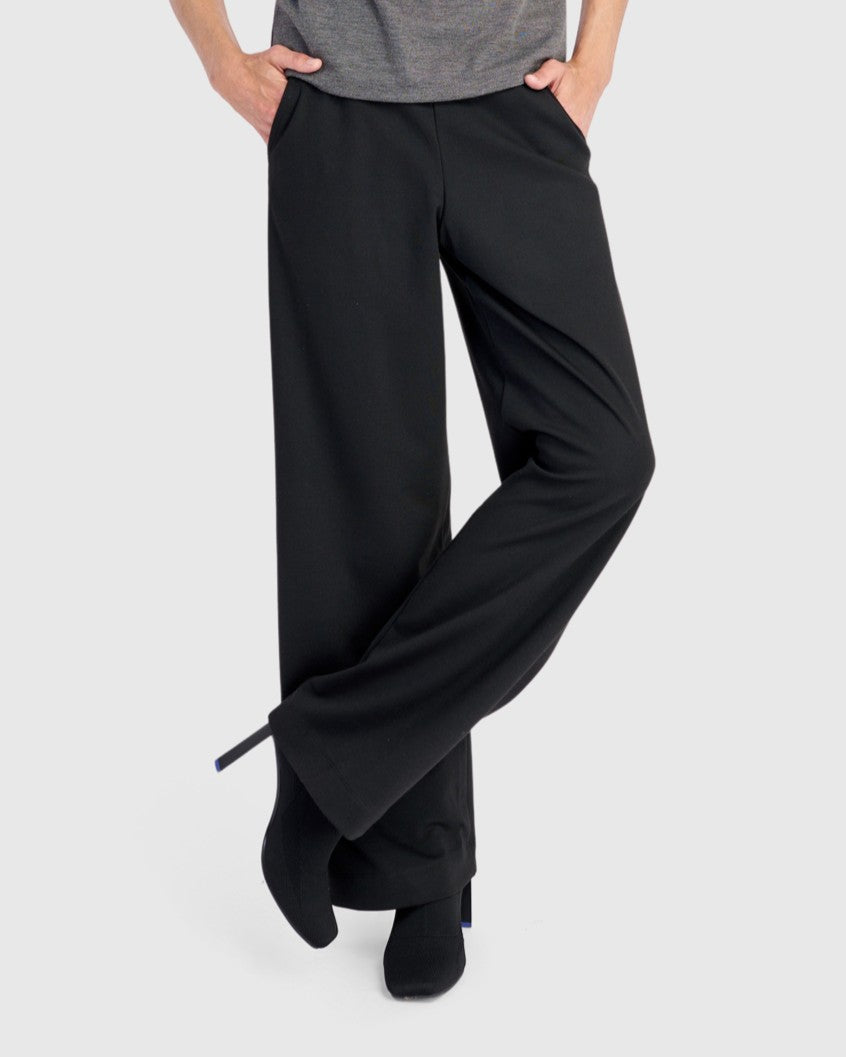 Wide-leg black pull-on trousers with side pockets, worn with black ankle boots, side view