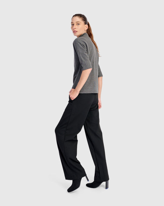Wide-leg black pull-on trousers with straight cut, worn with heeled boots, three-quarter back view
