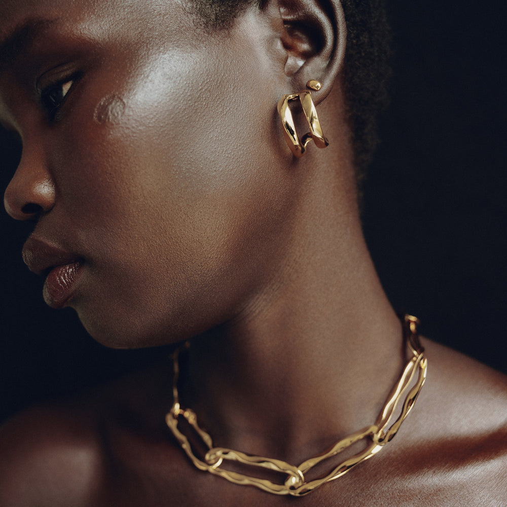 Gold hoop earrings worn on model's ear, chunky twisted design with reflective finish