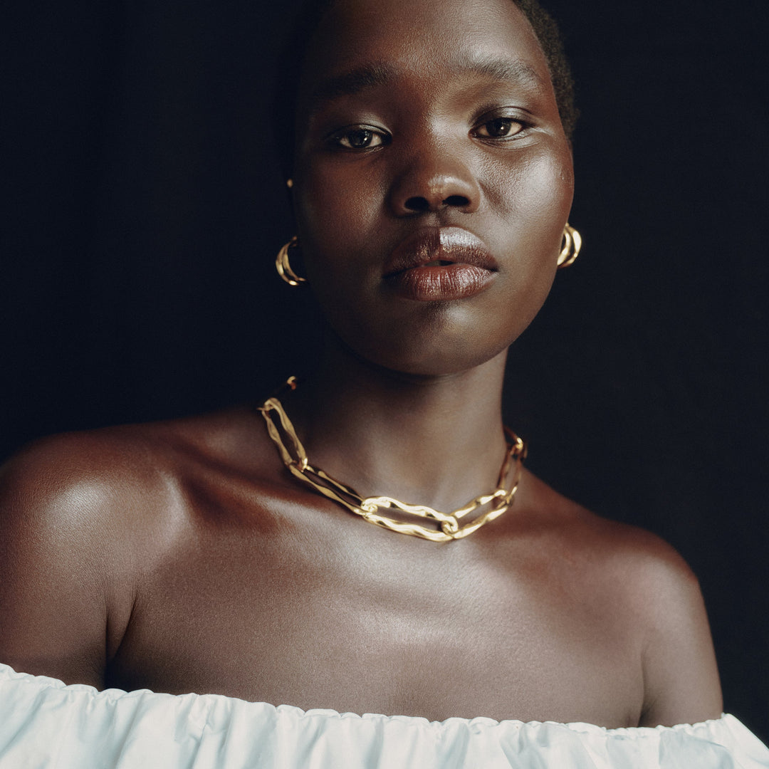 Gold hoop earrings worn by model with matching chain necklace against dark background