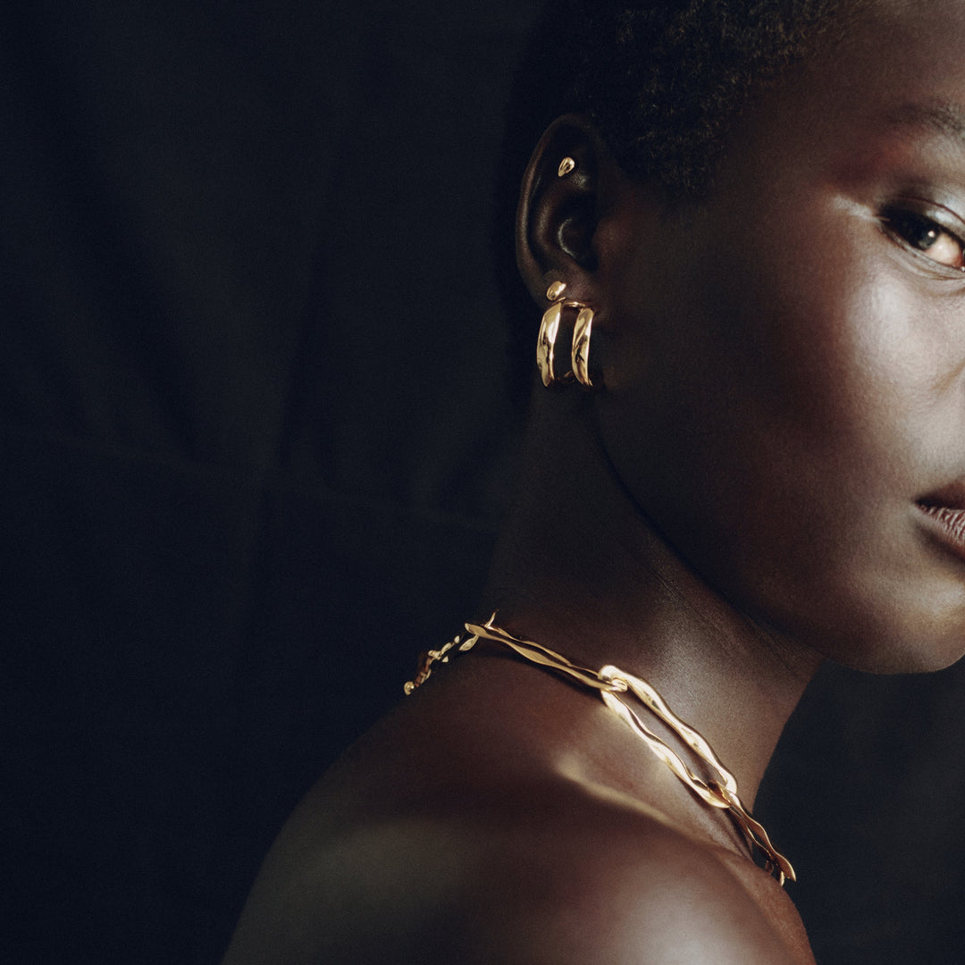 Gold hoop earrings worn by model in dramatic lighting, side profile view