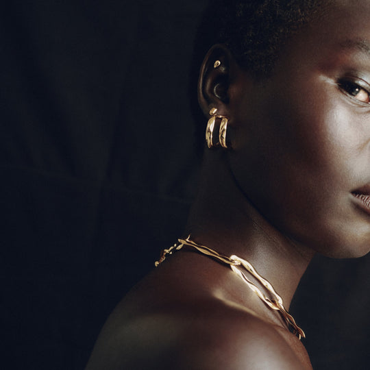 Gold hoop earrings worn by model in dramatic lighting, side profile view