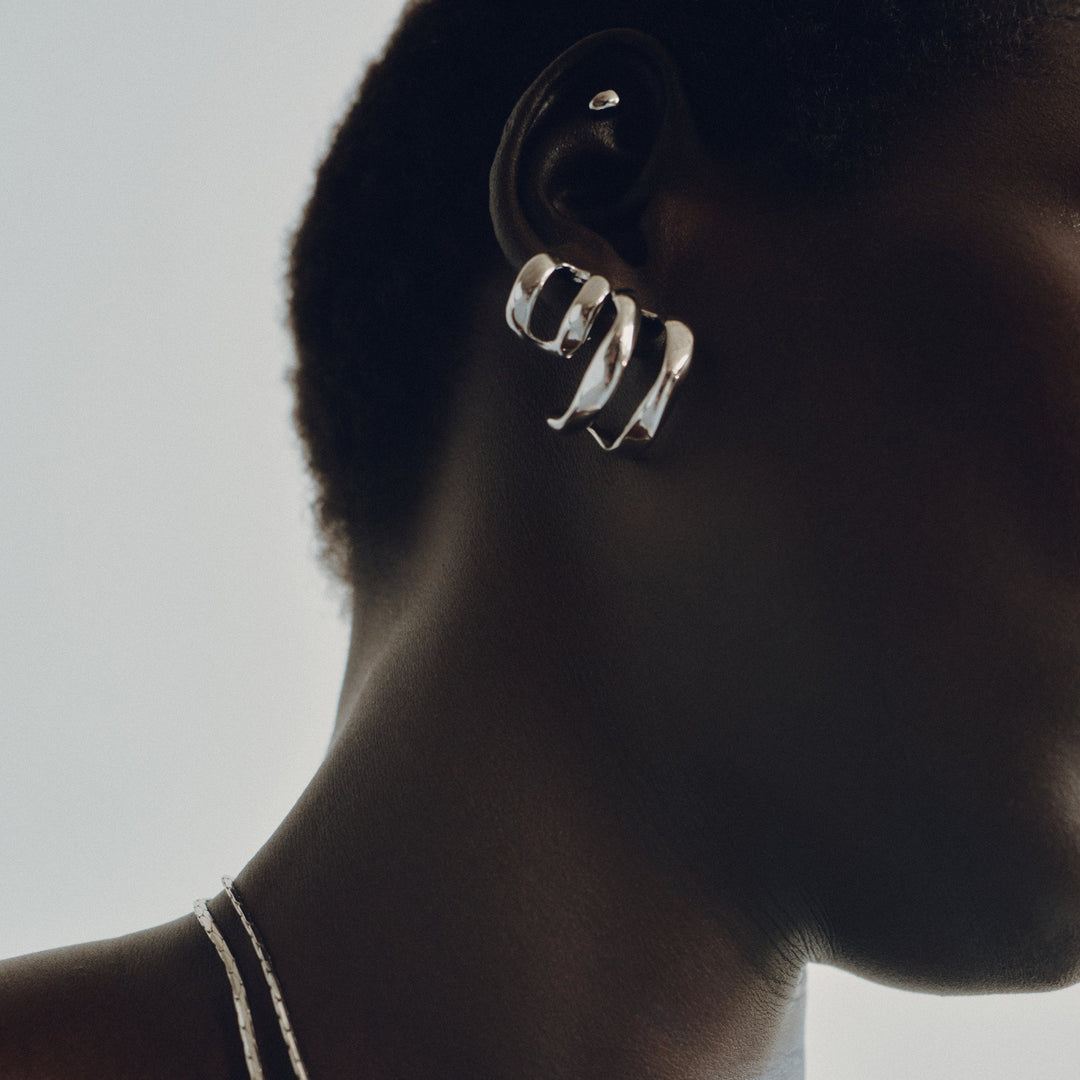 Chunky silver hoop earrings with twisted sculptural design worn on model's ear