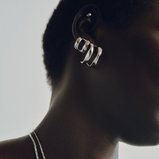 Chunky silver hoop earrings with twisted sculptural design worn on model's ear