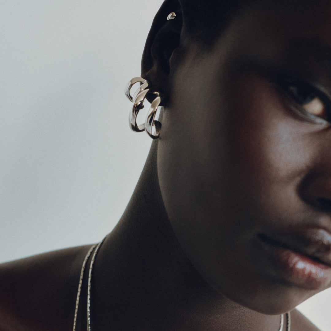 Twisted metallic hoop earrings worn on model's ear, side profile view