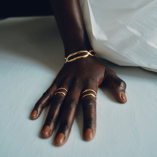 Gold rings worn on multiple fingers, hand resting on white bedding
