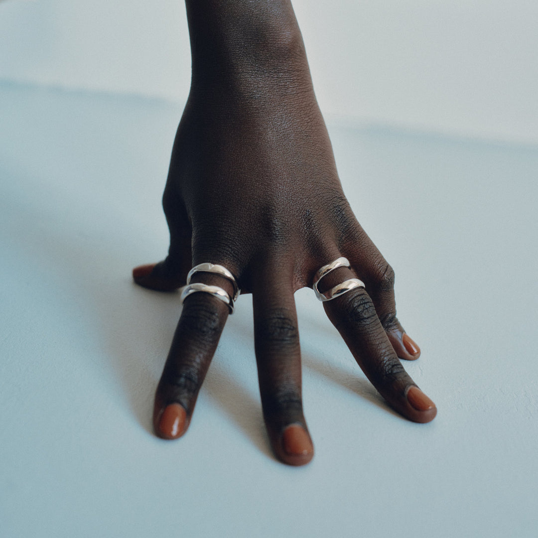 Hand wearing multiple silver rings on fingers against white background