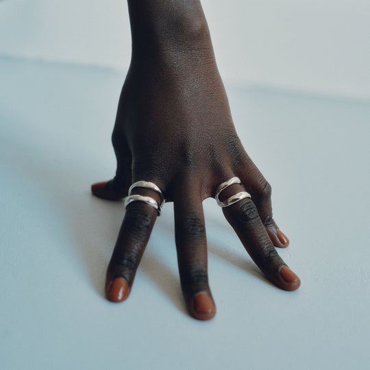 Hand wearing multiple silver rings on fingers against white background