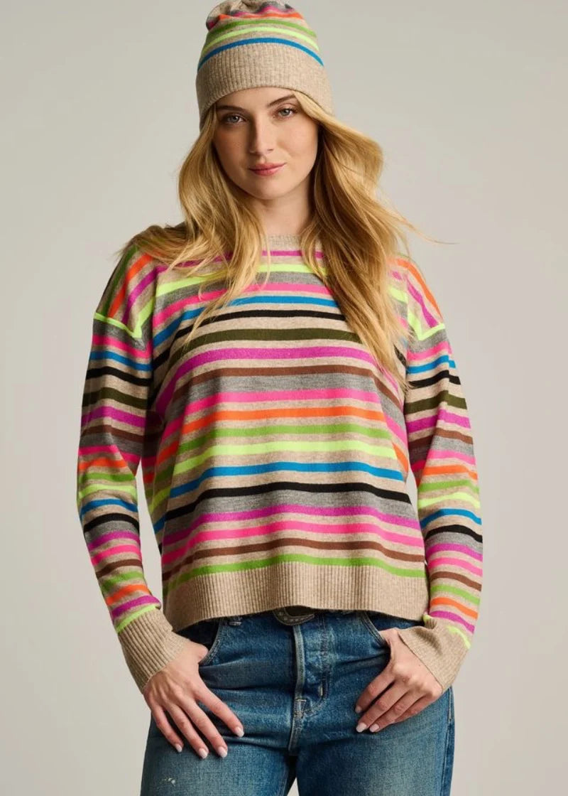 Woman wearing a colorful striped sweater and beanie against a plain background