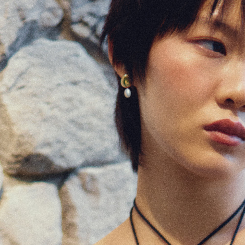 Gold crescent stud earrings with white pearl drops worn by model