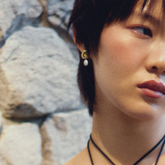 Gold crescent stud earrings with white pearl drops worn by model