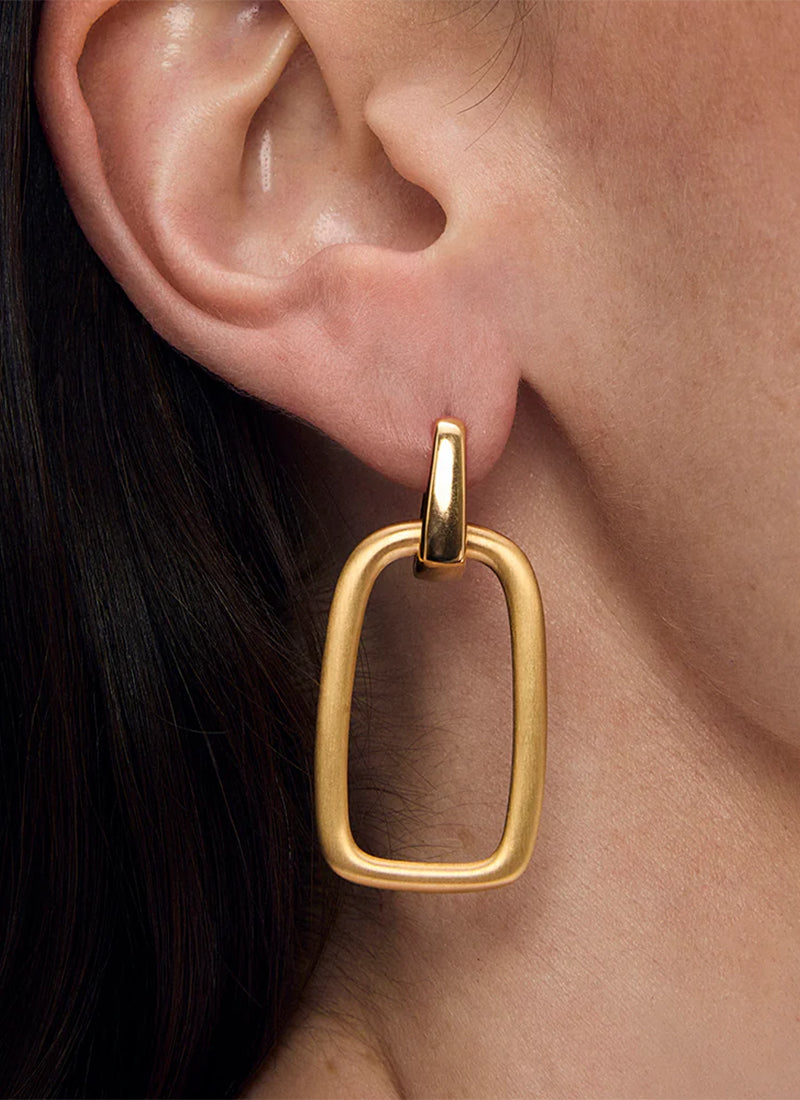 Gold drop hoop earring with open rectangular pendant worn on model's ear, side view