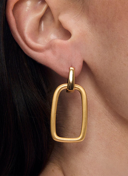 Gold drop hoop earring with open rectangular pendant worn on model's ear, side view