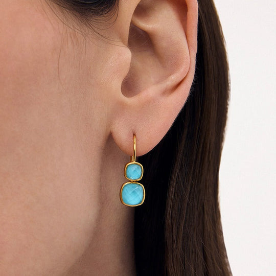Gold drop earrings with two turquoise gemstone cushion cuts worn on model's ear