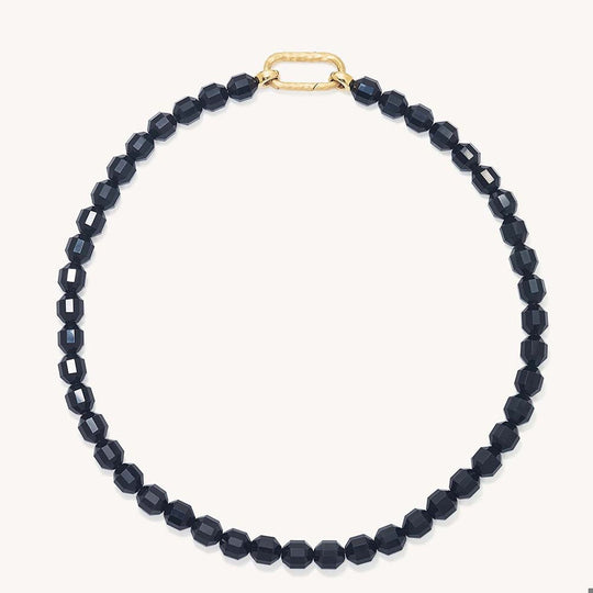 Faceted black beaded necklace laid flat in circle with gold carabiner-style clasp