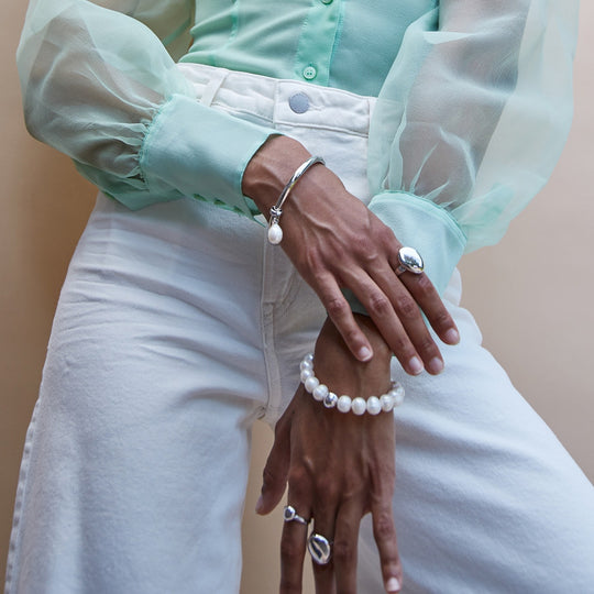 Silver pearl charm bracelet with bead strand and dangling silver charms on wrist